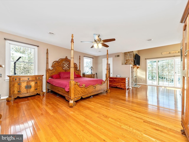 bedroom with ceiling fan, a fireplace, and light hardwood / wood-style flooring