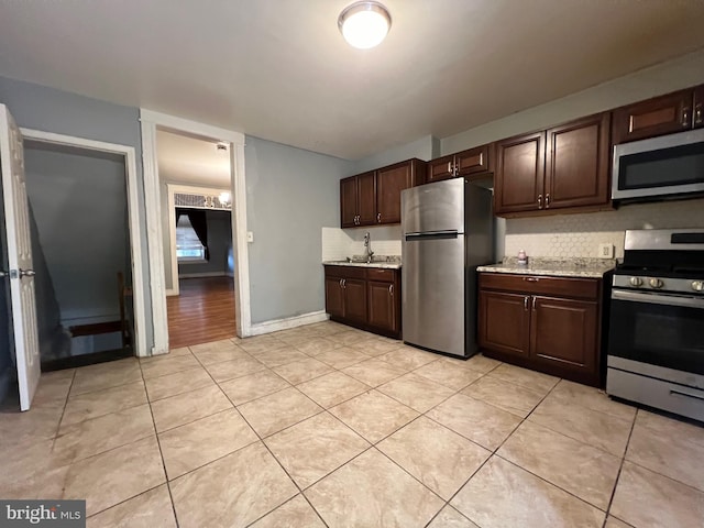 kitchen featuring stainless steel appliances, light stone counters, decorative backsplash, dark brown cabinets, and light tile patterned flooring