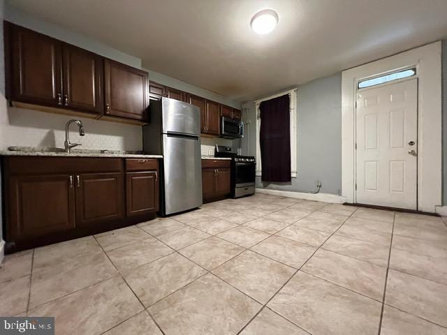 kitchen with light stone countertops, appliances with stainless steel finishes, dark brown cabinetry, sink, and light tile patterned floors