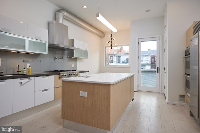 kitchen with white cabinetry, backsplash, hanging light fixtures, a center island, and wall chimney exhaust hood