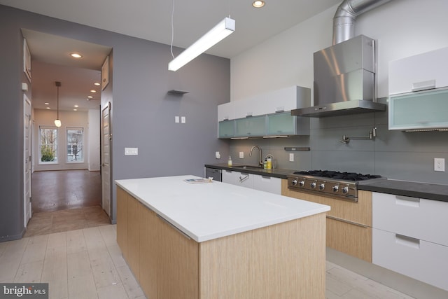 kitchen featuring hanging light fixtures, a center island, wall chimney exhaust hood, white cabinets, and stainless steel gas stovetop