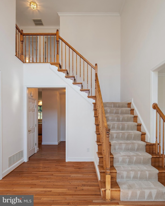 stairs featuring baseboards, wood finished floors, visible vents, and crown molding