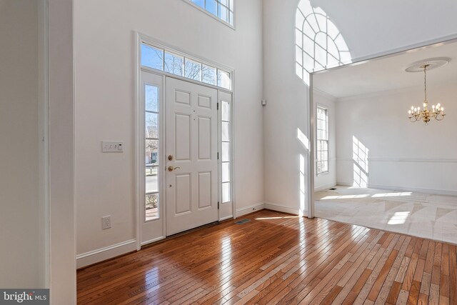 entrance foyer with baseboards, hardwood / wood-style floors, a towering ceiling, and an inviting chandelier