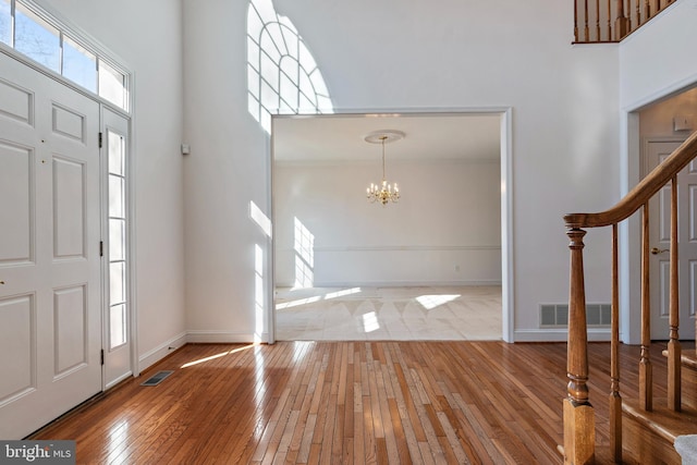 entrance foyer with stairs, wood-type flooring, visible vents, and a notable chandelier