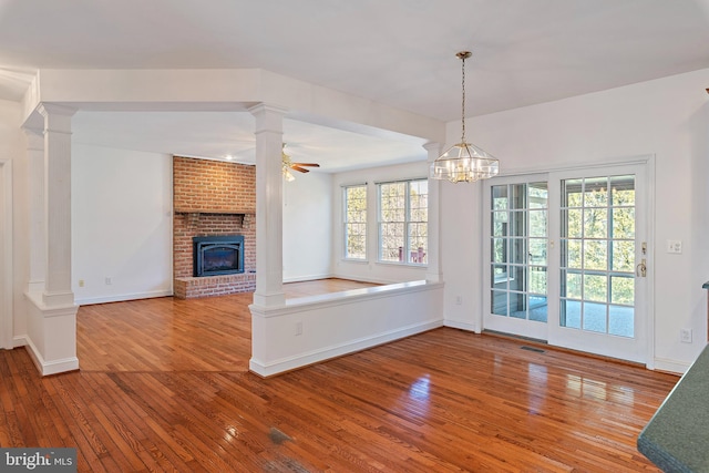 unfurnished living room with hardwood / wood-style flooring, decorative columns, a brick fireplace, and ceiling fan