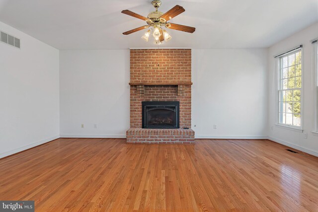 unfurnished living room featuring visible vents, light wood-style floors, a ceiling fan, a brick fireplace, and baseboards