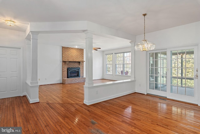 unfurnished living room with ornate columns, wood-type flooring, a brick fireplace, and baseboards