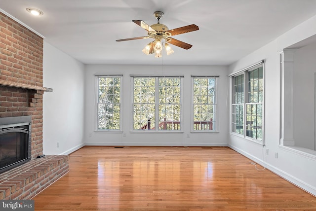 unfurnished living room featuring a brick fireplace, wood finished floors, a wealth of natural light, and baseboards