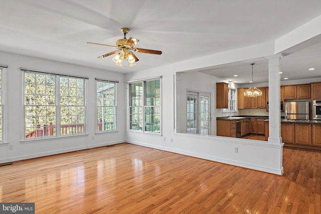 unfurnished living room with baseboards, light wood-type flooring, ornate columns, a sink, and ceiling fan with notable chandelier