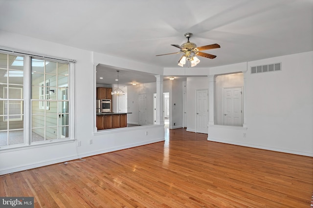 unfurnished living room featuring light wood-type flooring, visible vents, ceiling fan, and ornate columns