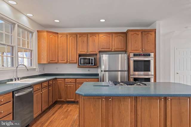 kitchen with light wood finished floors, dark countertops, appliances with stainless steel finishes, brown cabinets, and a sink