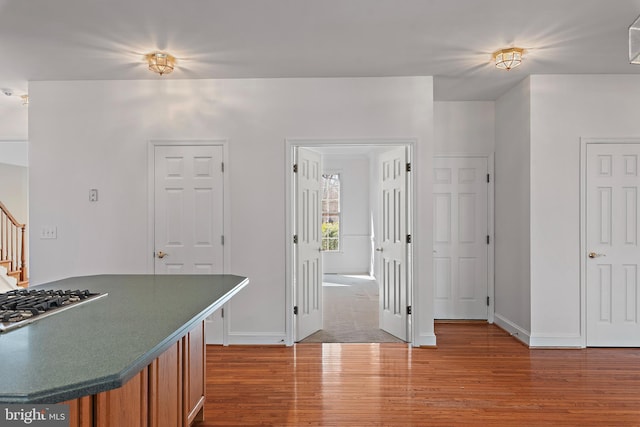 kitchen featuring brown cabinets, stainless steel gas cooktop, dark countertops, wood finished floors, and baseboards