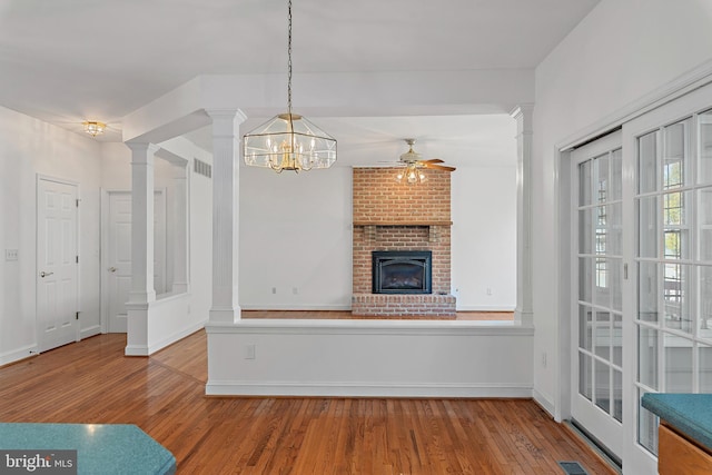 unfurnished living room with a fireplace, ornate columns, visible vents, wood finished floors, and baseboards