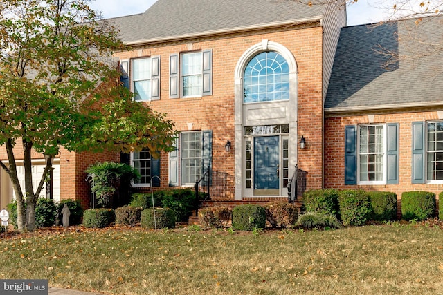 view of front of property with brick siding, a front yard, and a shingled roof