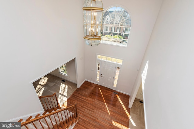 entryway with a chandelier, wood finished floors, a towering ceiling, and a healthy amount of sunlight