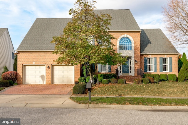 view of front facade featuring roof with shingles, brick siding, decorative driveway, and a front yard