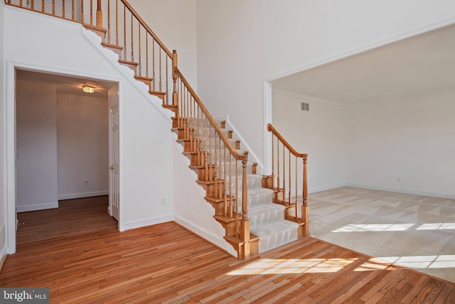 stairway featuring a high ceiling, visible vents, baseboards, hardwood / wood-style floors, and crown molding