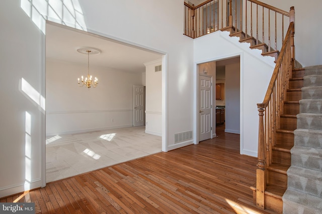 foyer entrance featuring visible vents, stairs, a high ceiling, light wood-style floors, and a notable chandelier