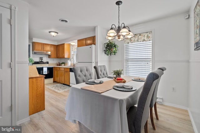 dining space with sink, an inviting chandelier, and light hardwood / wood-style flooring