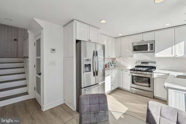 kitchen with light wood-type flooring, appliances with stainless steel finishes, white cabinetry, and tasteful backsplash