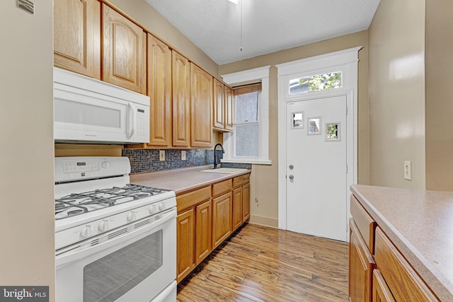 kitchen with a sink, tasteful backsplash, white appliances, light wood-style floors, and light countertops