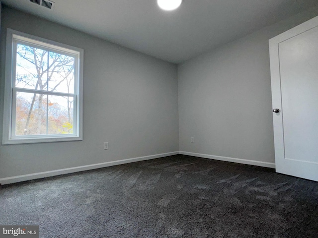 unfurnished room with baseboards and dark carpet