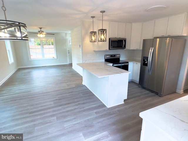 kitchen featuring wood finished floors, a peninsula, stainless steel appliances, hanging light fixtures, and white cabinets