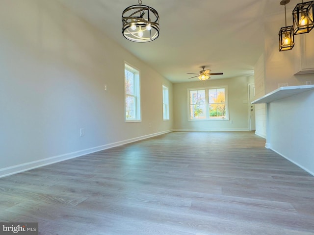 unfurnished living room with ceiling fan with notable chandelier, wood finished floors, and baseboards