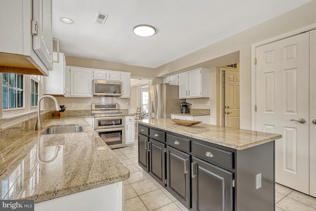 kitchen featuring stainless steel appliances, white cabinetry, a kitchen island, and sink