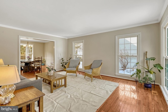 living room with an inviting chandelier, crown molding, light hardwood / wood-style flooring, and plenty of natural light