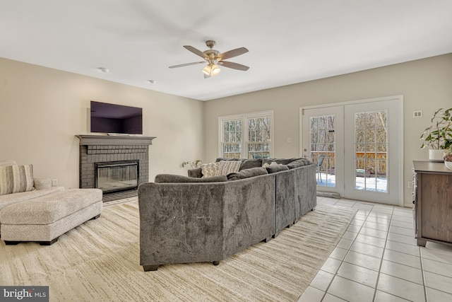 living room with a brick fireplace, light tile patterned floors, a healthy amount of sunlight, and ceiling fan