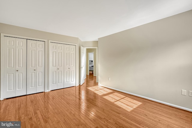 unfurnished bedroom featuring light wood-type flooring and multiple closets