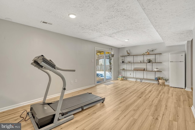 exercise area with light hardwood / wood-style floors and a textured ceiling