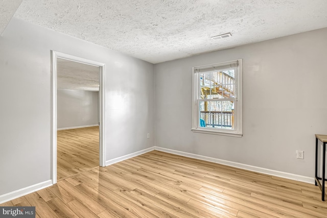 empty room with a textured ceiling and light hardwood / wood-style floors