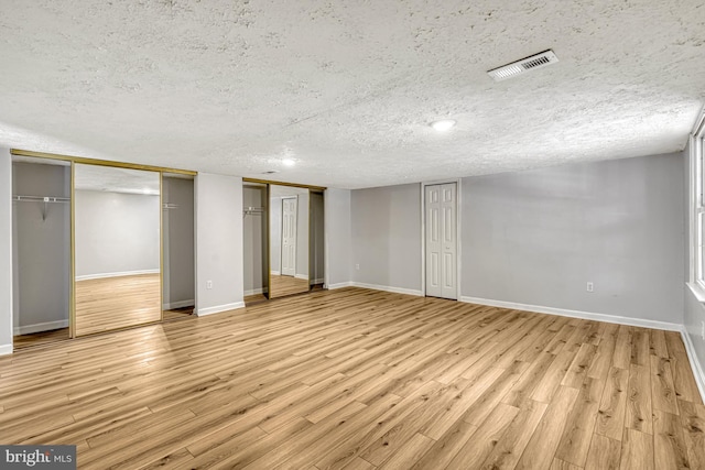 unfurnished bedroom featuring a textured ceiling, two closets, and light hardwood / wood-style flooring