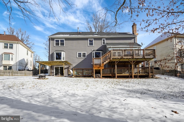 snow covered back of property with a wooden deck and a fire pit