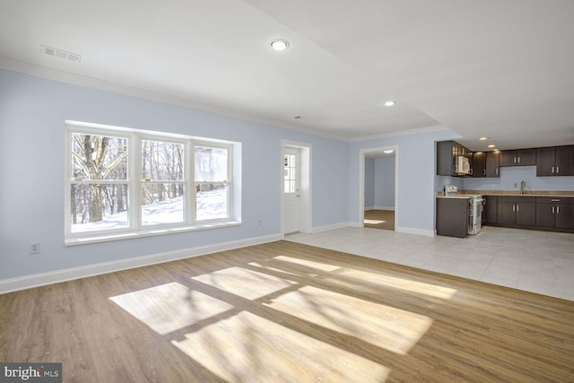 unfurnished living room with sink, light wood-type flooring, ornamental molding, and a wealth of natural light