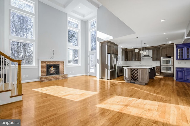 unfurnished living room featuring coffered ceiling, a high ceiling, a brick fireplace, and light hardwood / wood-style flooring