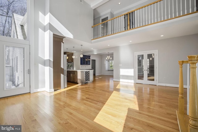 unfurnished living room with a high ceiling, french doors, light hardwood / wood-style floors, and a chandelier