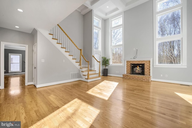 unfurnished living room with coffered ceiling, a high ceiling, a fireplace, and light hardwood / wood-style floors