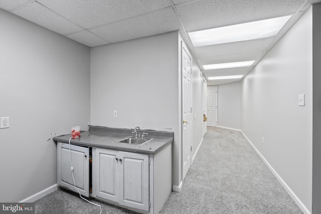 hallway with a drop ceiling, light colored carpet, and sink