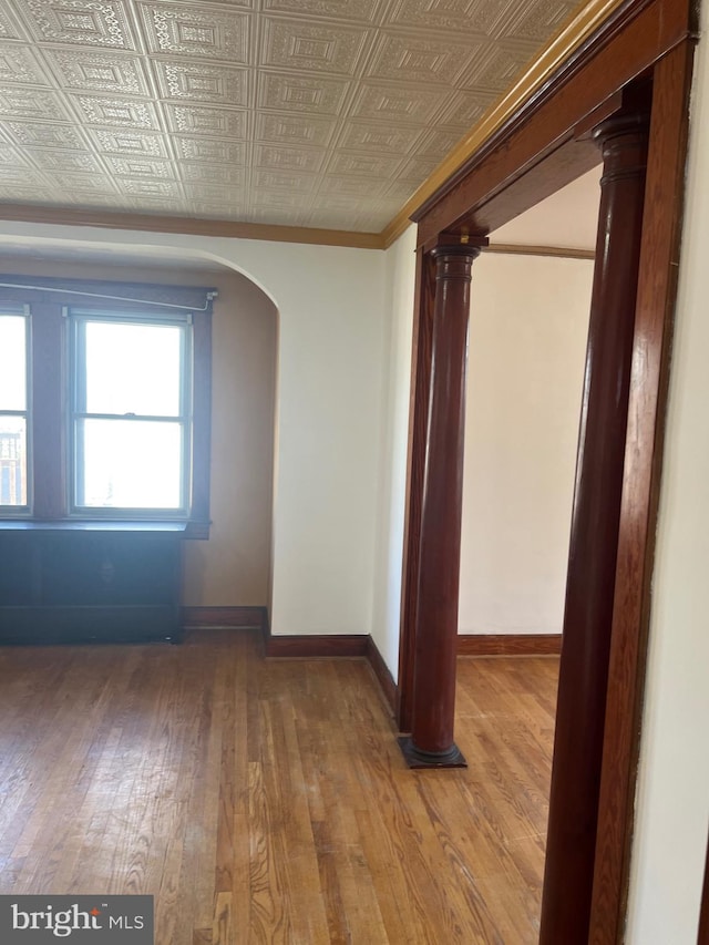 empty room with ornamental molding, an ornate ceiling, arched walkways, wood-type flooring, and baseboards