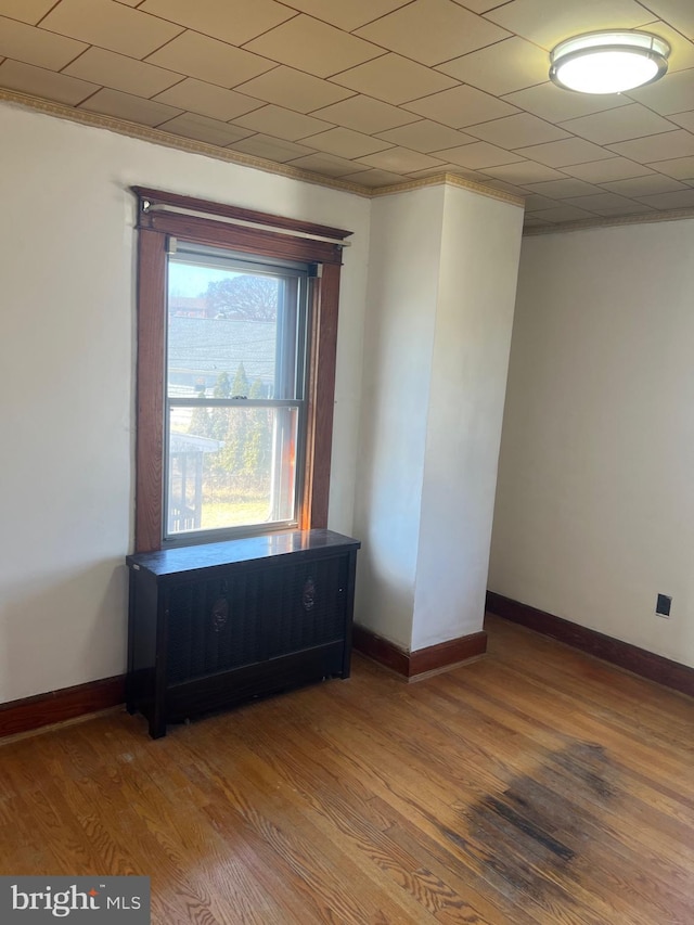 empty room featuring crown molding, wood finished floors, and baseboards