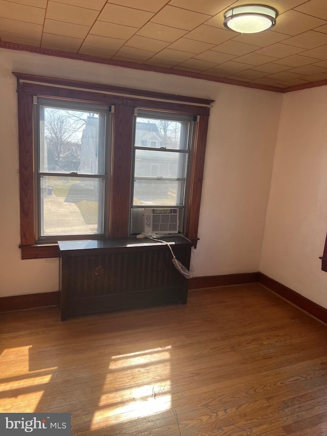 unfurnished room with ornamental molding, cooling unit, baseboards, and wood finished floors