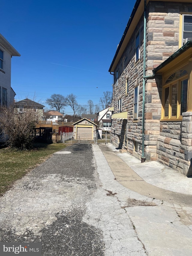 view of side of property featuring a garage, stone siding, an outdoor structure, and driveway