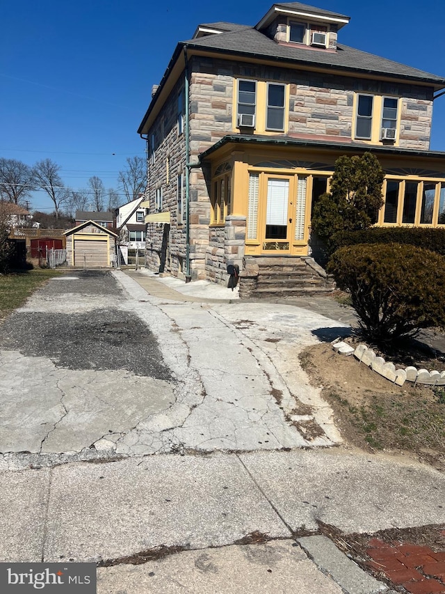 american foursquare style home featuring an outbuilding, stone siding, and driveway