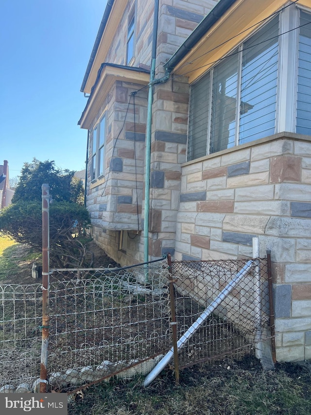 view of side of home featuring stone siding and fence