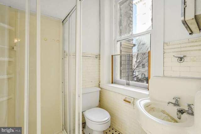 bathroom with sink, toilet, a shower with door, and tile walls