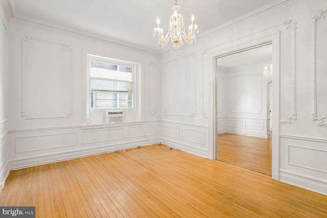 spare room featuring hardwood / wood-style floors, cooling unit, ornamental molding, and a chandelier