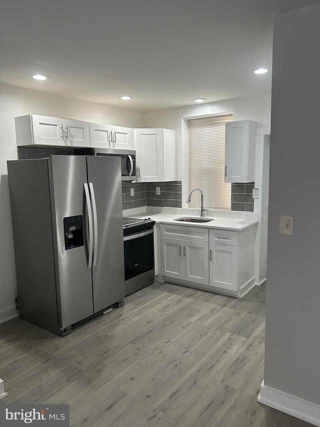 kitchen with appliances with stainless steel finishes, light countertops, light wood-style floors, white cabinetry, and a sink